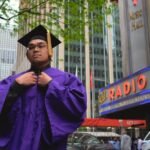 man wearing purple and black educational gown standing near building